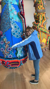 A girl posing with a colorful fabric installation, acting as if she was hugging it